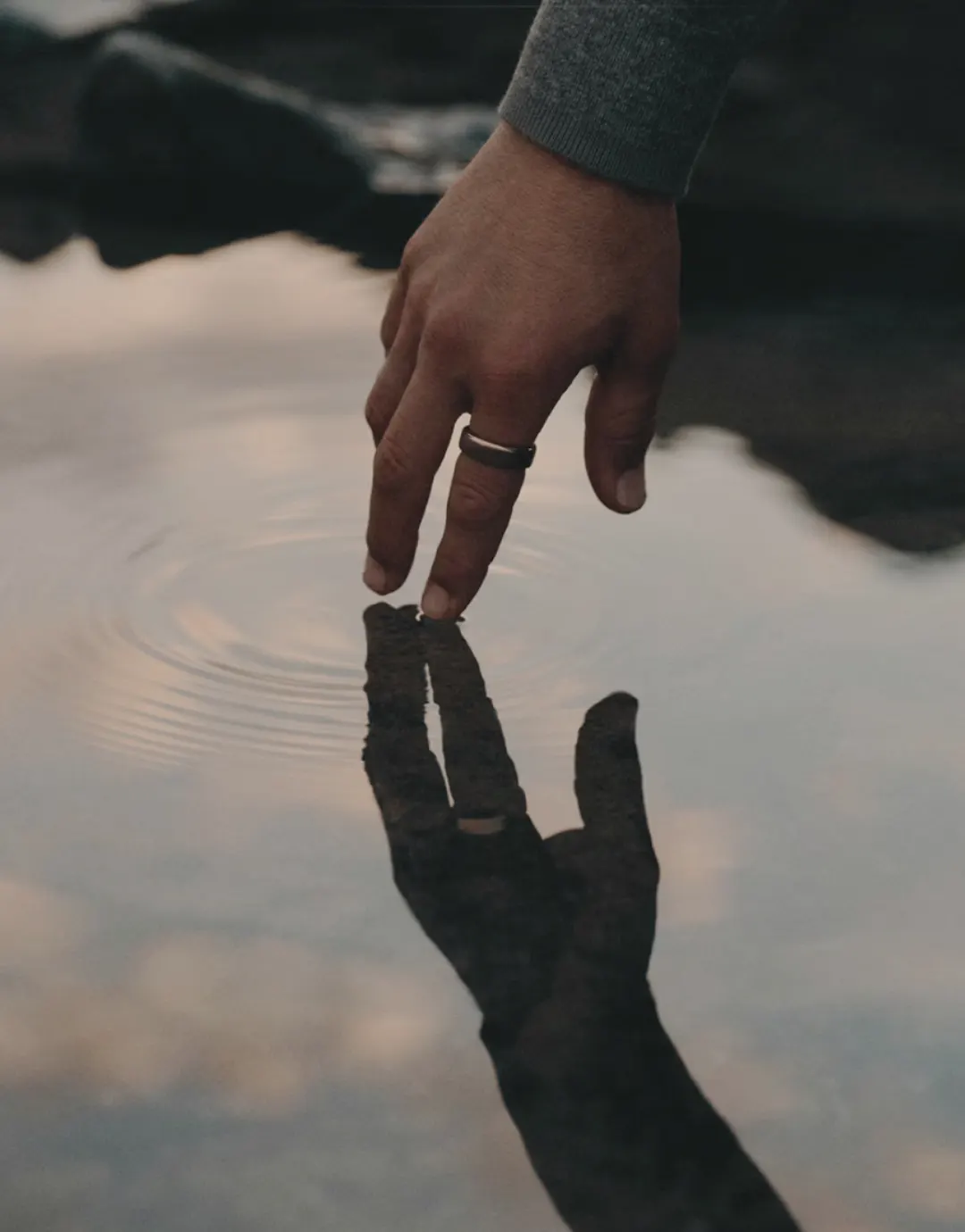 Mano rozando el agua y su reflejo